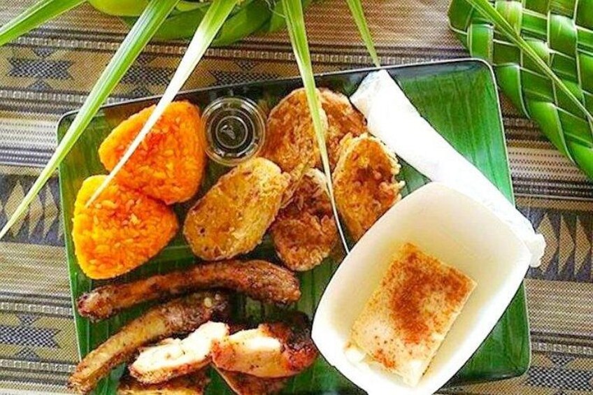 Variedad de alimentos fritos en un plato verde, incluyendo rodajas de fruta anaranjada, pollo frito y un recipiente pequeño con salsa blanca. 5