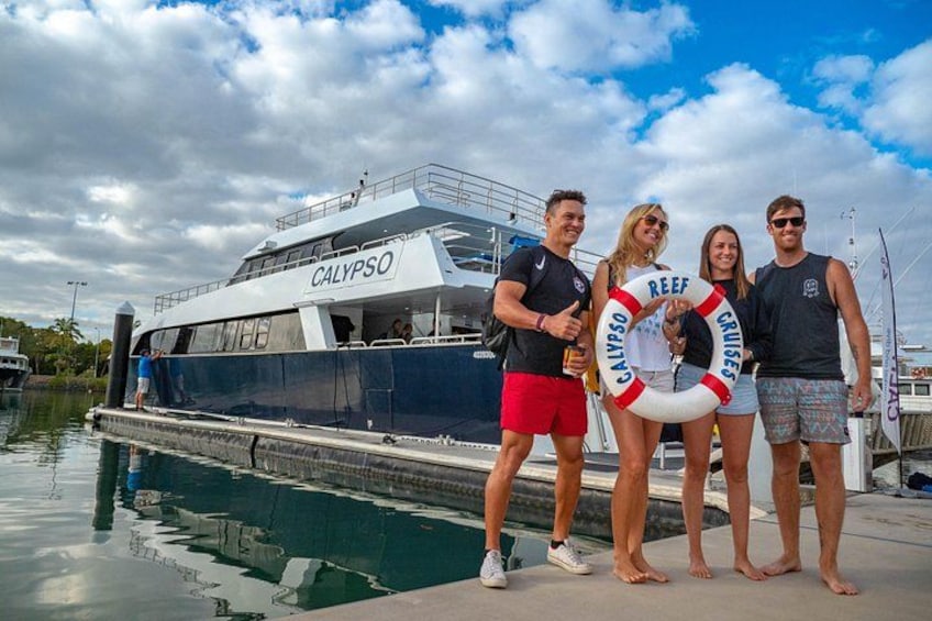 A boat named CALYPSO docked at a marina with a lifebuoy labeled 'REEF CRUISE' and a group of people standing on the dock. 2
