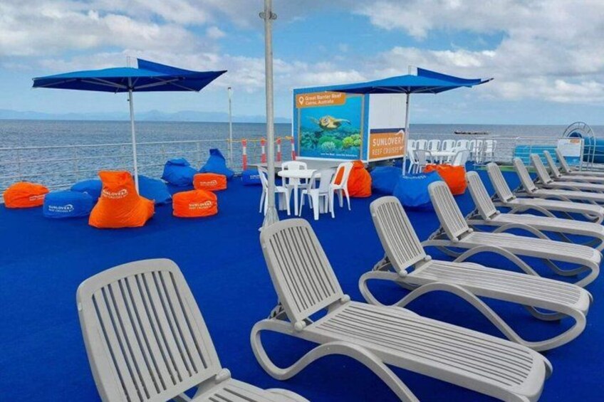 A deck with lounge chairs and bean bags, a signboard, and the ocean in the background. 3