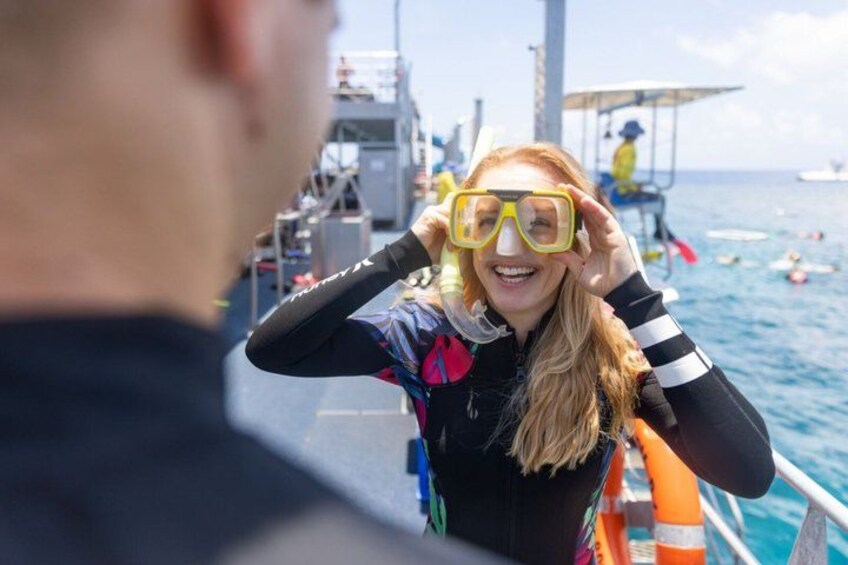 A person wearing a wetsuit and snorkeling gear, standing on a boat with the ocean in the background. 5