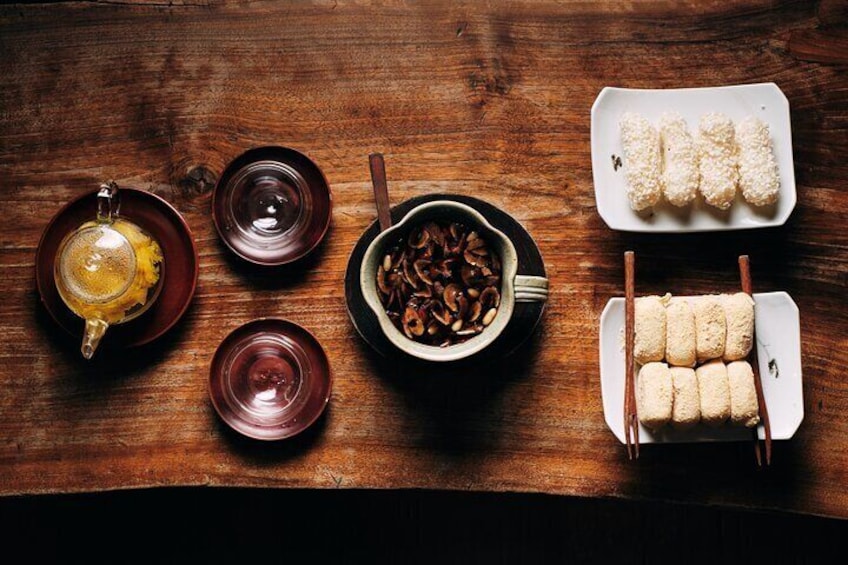 A wooden table with various dishes, including a teapot, bowls, and a tray of food. 1
