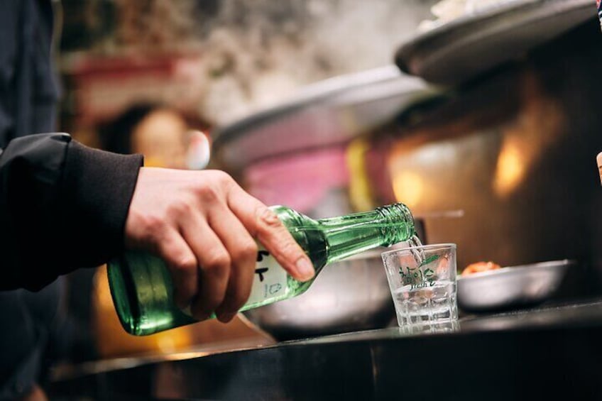 A hand pouring a green liquid from a bottle into a glass. 4