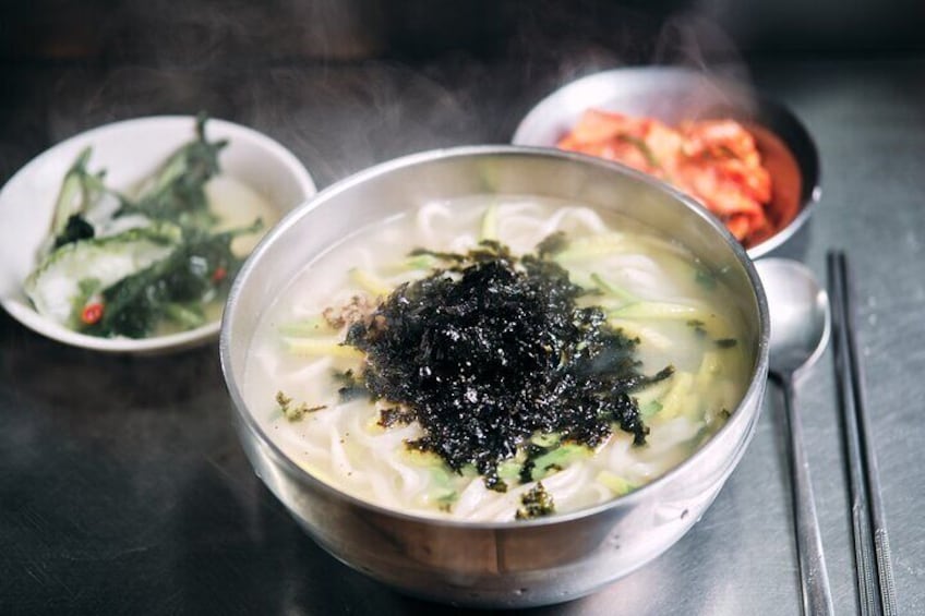A bowl of noodle soup garnished with seaweed, accompanied by side dishes. 2