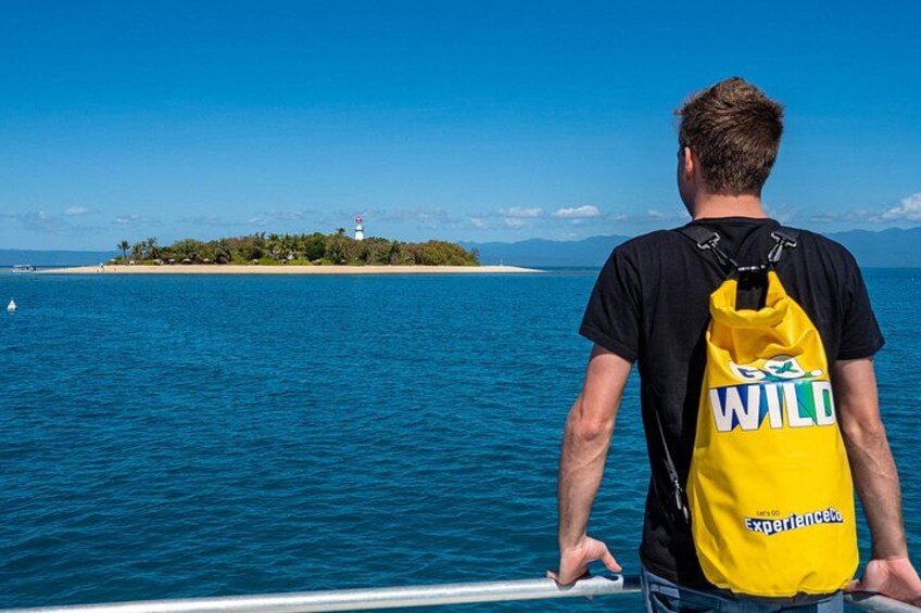 Een persoon in een boot, met een gele tas met de tekst 'WILD Experience', kijkt naar een vuurtoren op een klein eiland. 3