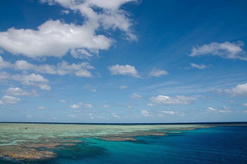A coastal landscape with clear blue water, a sandy beach, and a partly cloudy sky. 4
