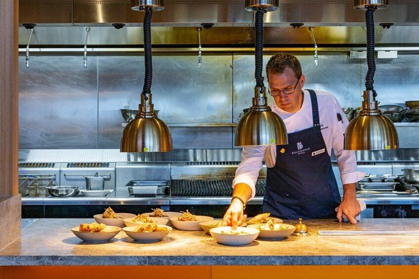 Un chef preparando comida en una cocina profesional con electrodomésticos de acero inoxidable e iluminación colgante. 3