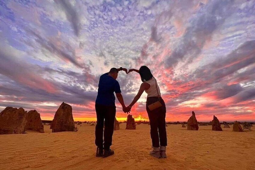 Two people holding hands in a desert landscape with rock formations and a sunset. 1