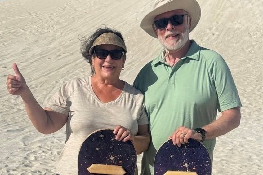 Two people holding star-patterned boards, standing on a sandy beach. 4