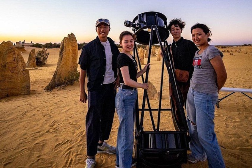 A group of people standing in a desert with a large camera on a tripod. 2