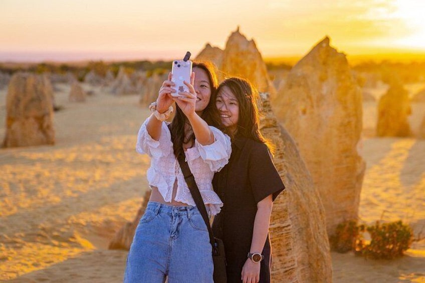 Two people taking a selfie with a smartphone in a desert landscape with large rock formations. 5