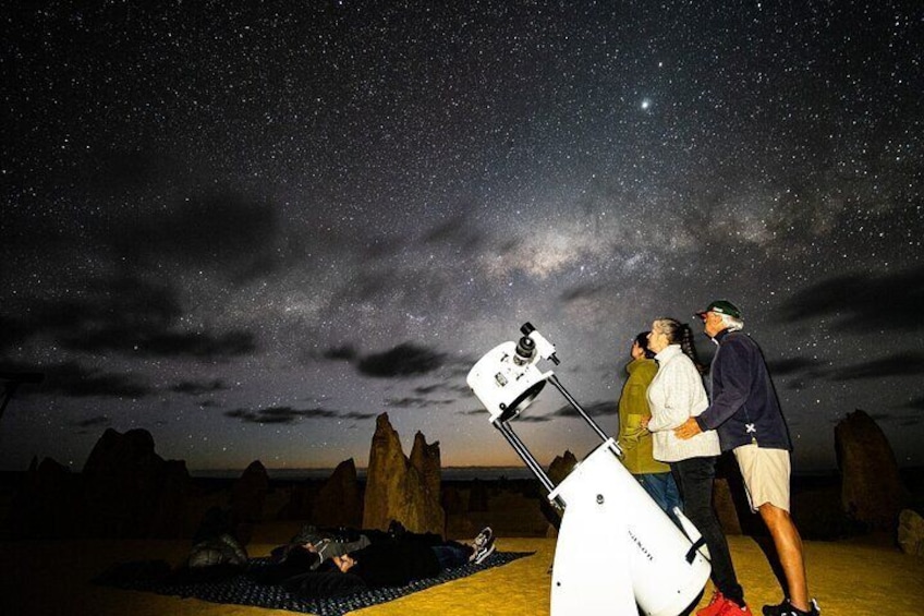 A starry night sky with a telescope, rocky terrain, and a person lying on the ground. 3