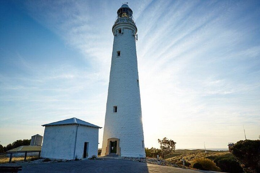 A tall white lighthouse with a small adjacent building, set against a clear sky. 1