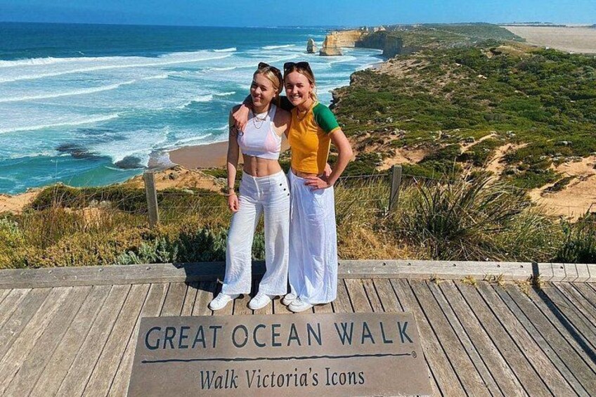 Two people standing on a wooden boardwalk with a sign that reads 'GREAT OCEAN WALK' and 'Walk Victoria's Icons'. 4