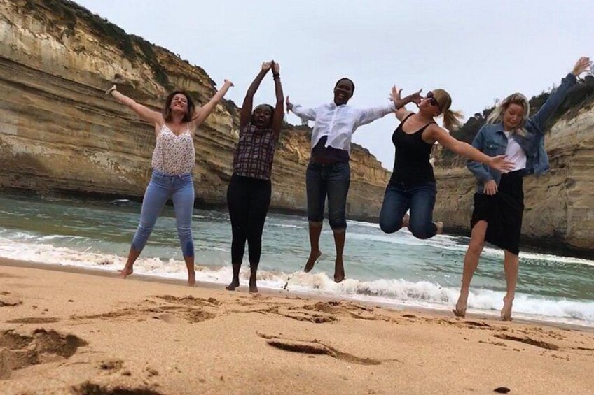 A group of people jumping on a sandy beach with cliffs in the background. 3