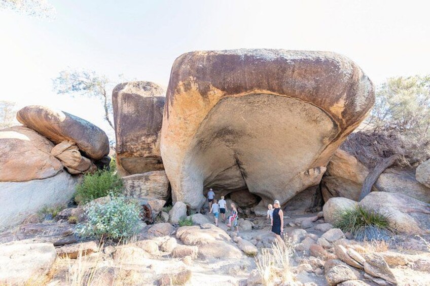Une grande formation rocheuse dotée d’une ouverture ressemblant à une grotte, entourée de rochers plus petits et d’une végétation clairsemée. 4