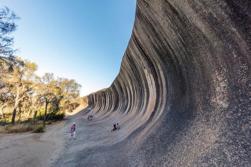 Une grande formation rocheuse à la surface incurvée, un sentier de terre et quelques personnes qui se promènent. 2