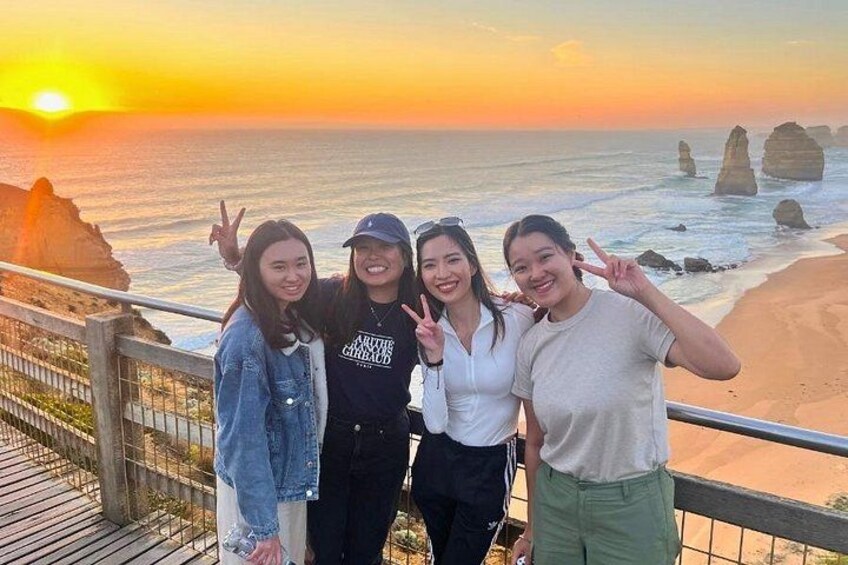 Four people posing on a wooden boardwalk with a sunset and rock formations in the background. 3