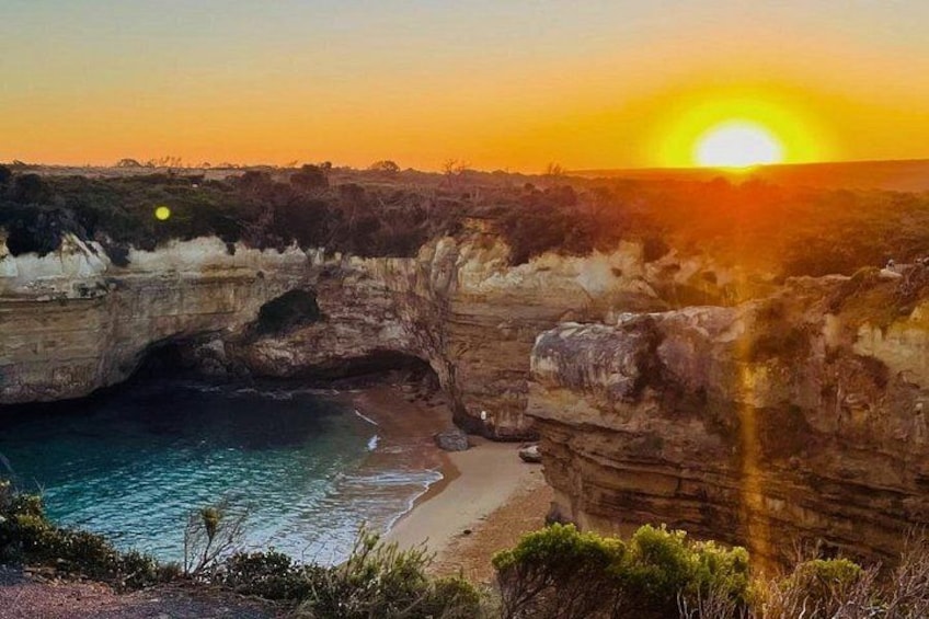 A coastal landscape with a large rock formation, a beach, and a sunset. 2