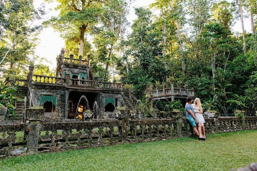 Una pareja abrazándose en un jardín exuberante con un puente de piedra y un pabellón. 1