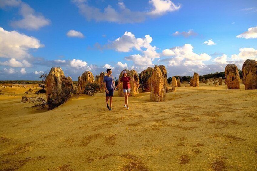 Two people walking on a sandy terrain with large rock formations in the background. 2