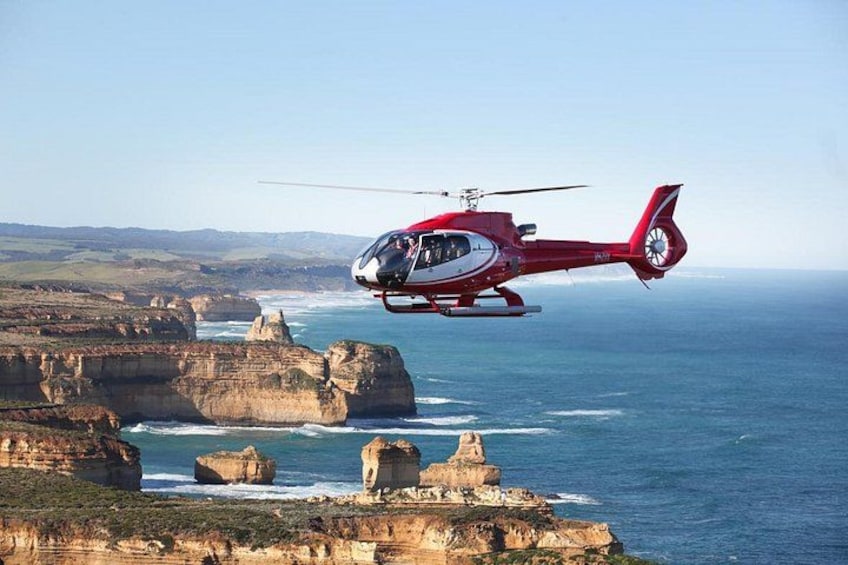 A red helicopter flying over a coastal landscape with cliffs and the ocean. 2
