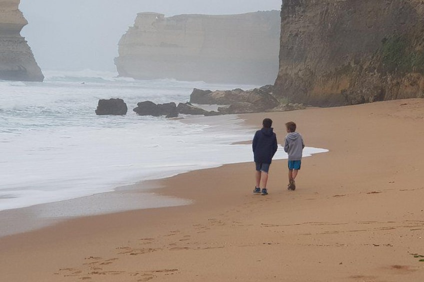 Two people walking on a sandy beach with rocky cliffs in the background. 3