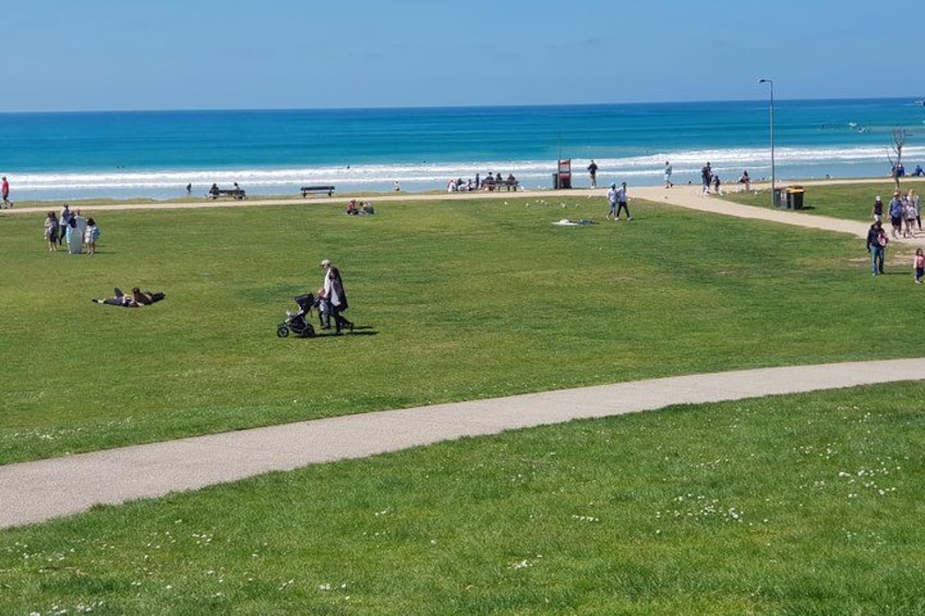 A grassy park with a path, people walking, and the ocean in the background. 3