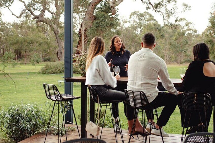 Un grupo de personas sentadas en una mesa al aire libre, con sillas, rodeado de follaje y árboles. 4
