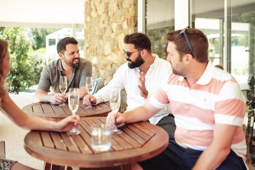 A group of people sitting at a wooden table outdoors, holding wine glasses. 3