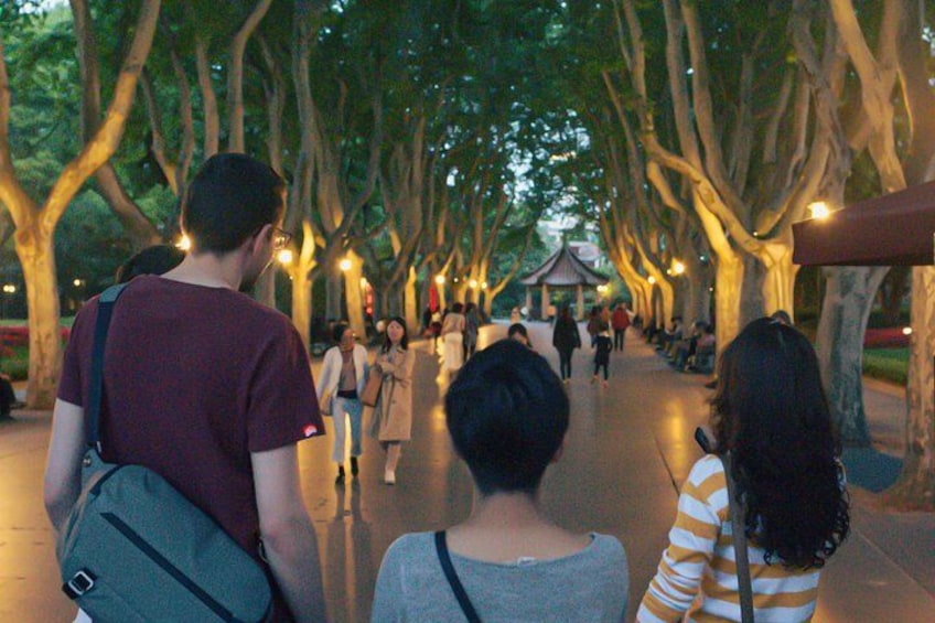 A tree-lined pathway with people walking, a gazebo in the distance, and street lamps. 3
