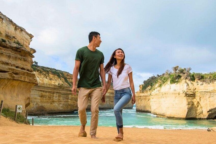 Ein Paar spaziert über einen sandigen Strand, im Hintergrund steilen Klippen. 3
