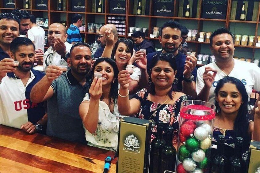 A group of people posing in a store with shelves of bottles and a display of Christmas ornaments. 2