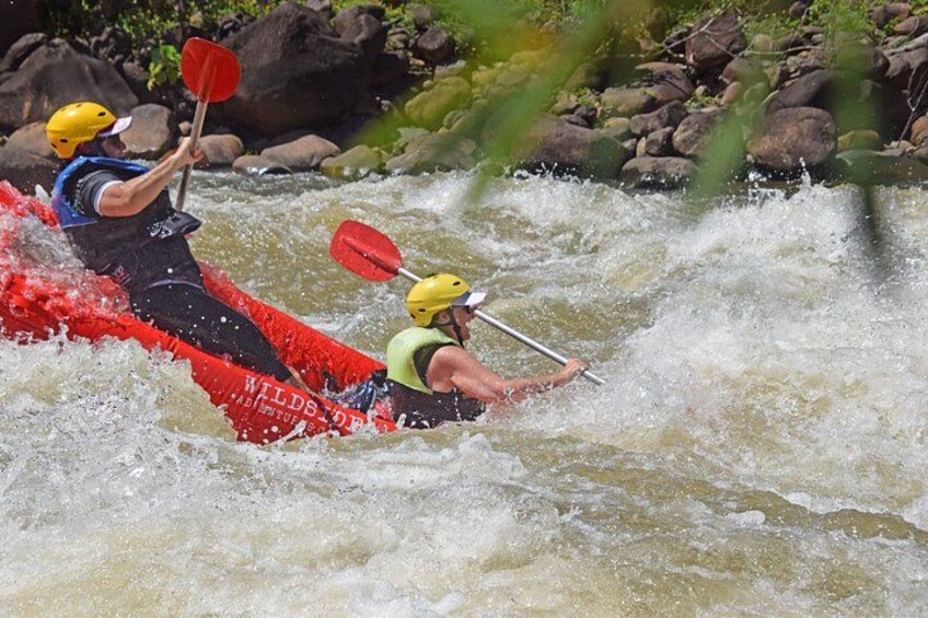 Two people kayaking on a river with rapids. 2
