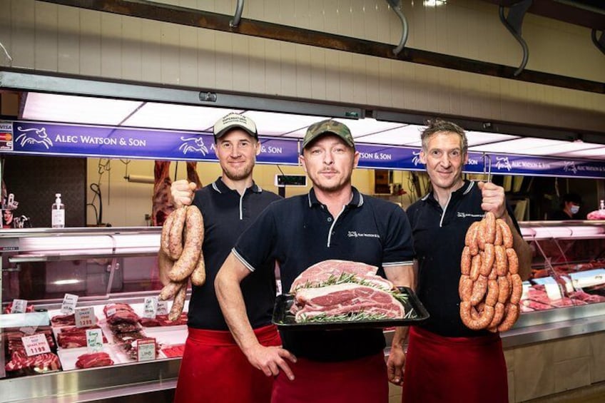 Three individuals in a butcher shop holding various meats. 2