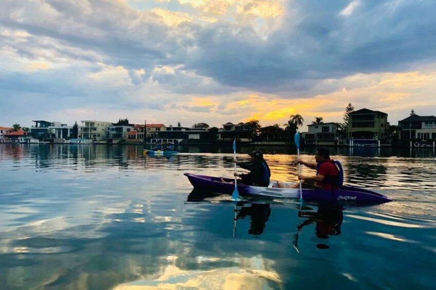 A sunset over a calm body of water with a kayak and a small boat. 2