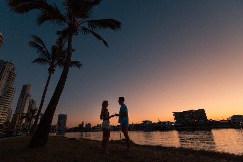 A sunset over a body of water with palm trees and buildings in the background. 3