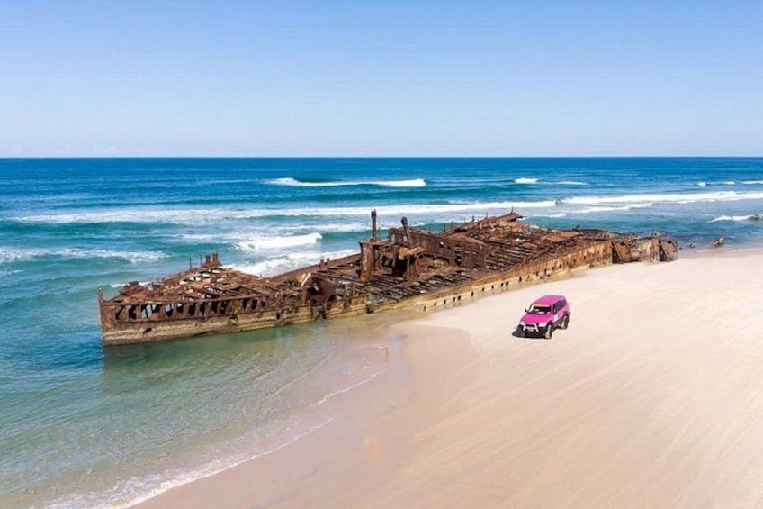 A shipwreck on a beach with a pink car parked nearby. 2