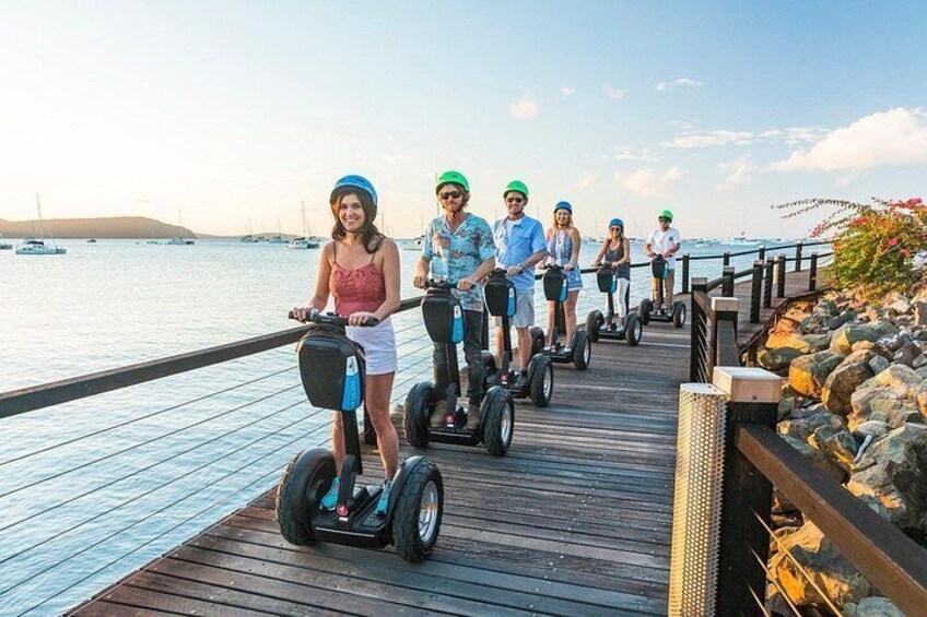 People riding segways on a wooden pier by the water. 5