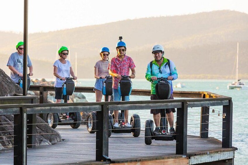 A group of people on hoverboards on a wooden dock by the water. 2