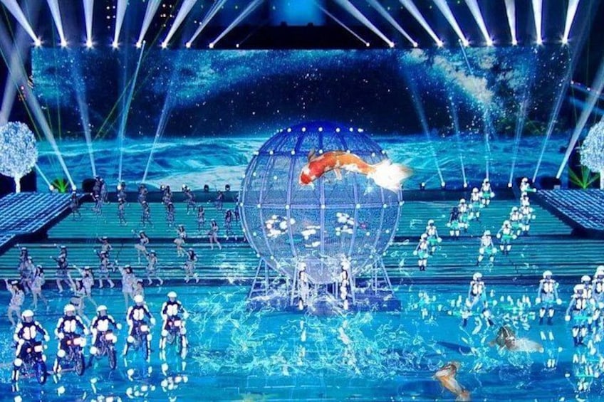A stage with performers in costumes, a large transparent sphere, and a water feature. 1