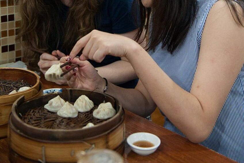 A person preparing dumplings on a table with a bowl of soup and a steaming pot. 3