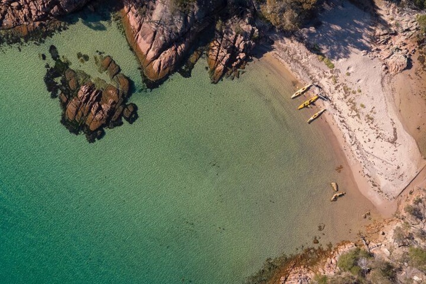 Un paysage côtier caractérisé par une eau turquoise cristalline, des formations rocheuses et une plage de sable où sont amarrés des bateaux jaunes. 1