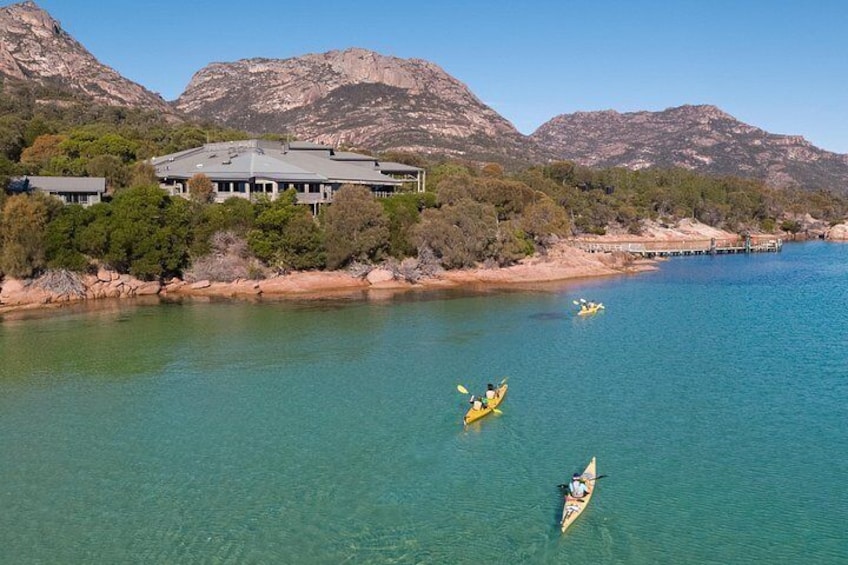 A river with kayaks, a house, and mountains in the background. 2