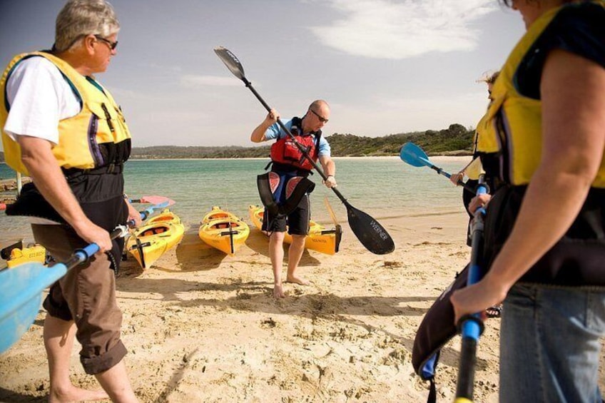 People on a beach with kayaks, a man paddling, and a calm sea. 3