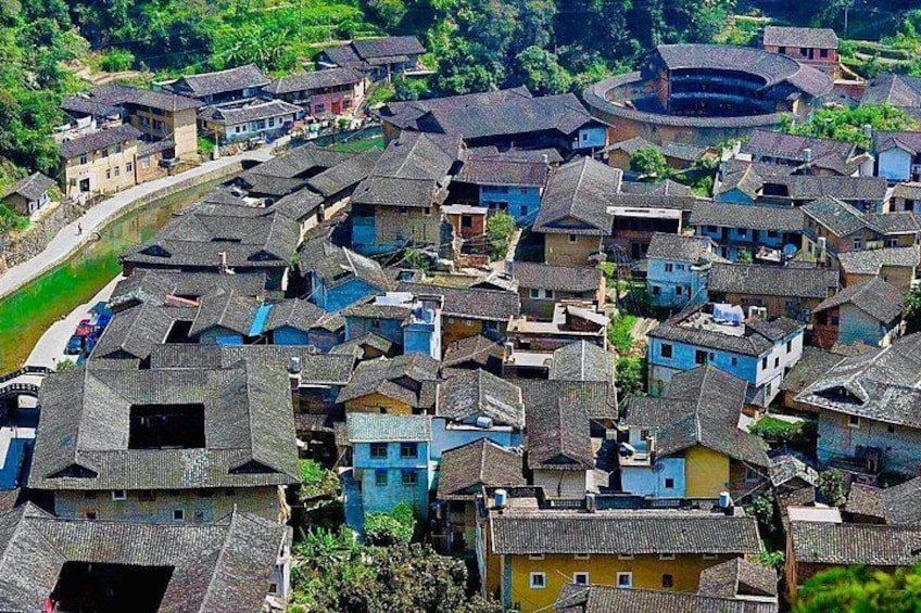 A densely packed village with traditional buildings, a river running through it, and a circular structure in the background. 1