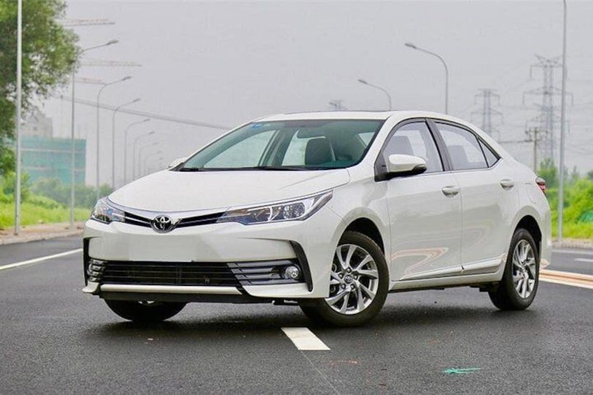 A white Toyota sedan parked on a road with a clear sky and greenery in the background. 5