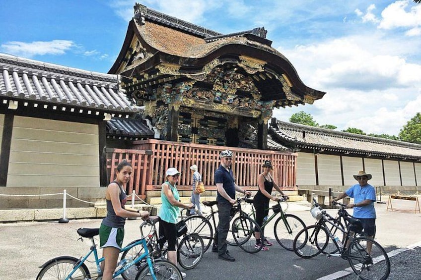 Un bâtiment traditionnel à l’architecture richement décorée, un groupe de personnes à vélo et un ciel dégagé. 2