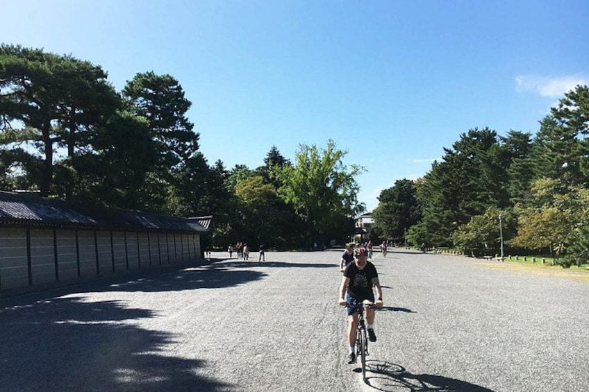 Un chemin de gravier bordé d’arbres, avec des cyclistes et un bâtiment en arrière-plan. 3