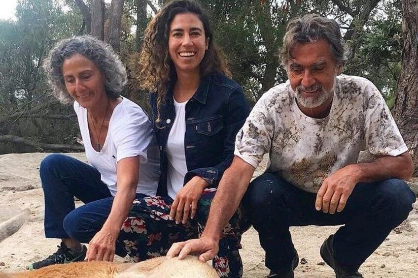 Three people sitting on a sandy beach with trees in the background. 2