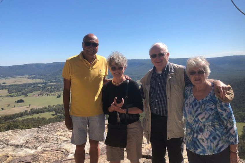 Quatre personnes se tiennent sur un promontoire rocheux, d’où l’on peut admirer une vallée et des collines lointaines. 4